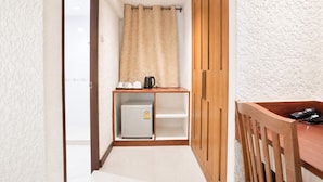 Un couloir avec une armoire en bois, une petite kitchenette équipée d’un réfrigérateur, et un bureau en bois avec une chaise.