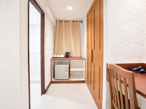 A hallway with a wooden wardrobe, a small kitchenette with a refrigerator, and a wooden desk with a chair. - Blue Neptuna Hotel Patong by Koko (Patong)