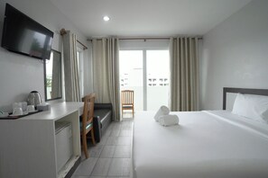 Ett hotellrum med en säng, ett skrivbord med en platt-TV, en stol, ett litet bord med en vattenkokare och koppar, och utsikt över omgivningarna genom ett stort fönster.
