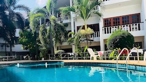 Une piscine entourée d’une clôture blanche, bordée de palmiers et donnant sur un immeuble doté de balcons.