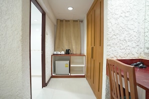 Um corredor estreito com um frigorífico branco, um armário de madeira e uma mesa vermelha com uma cadeira.