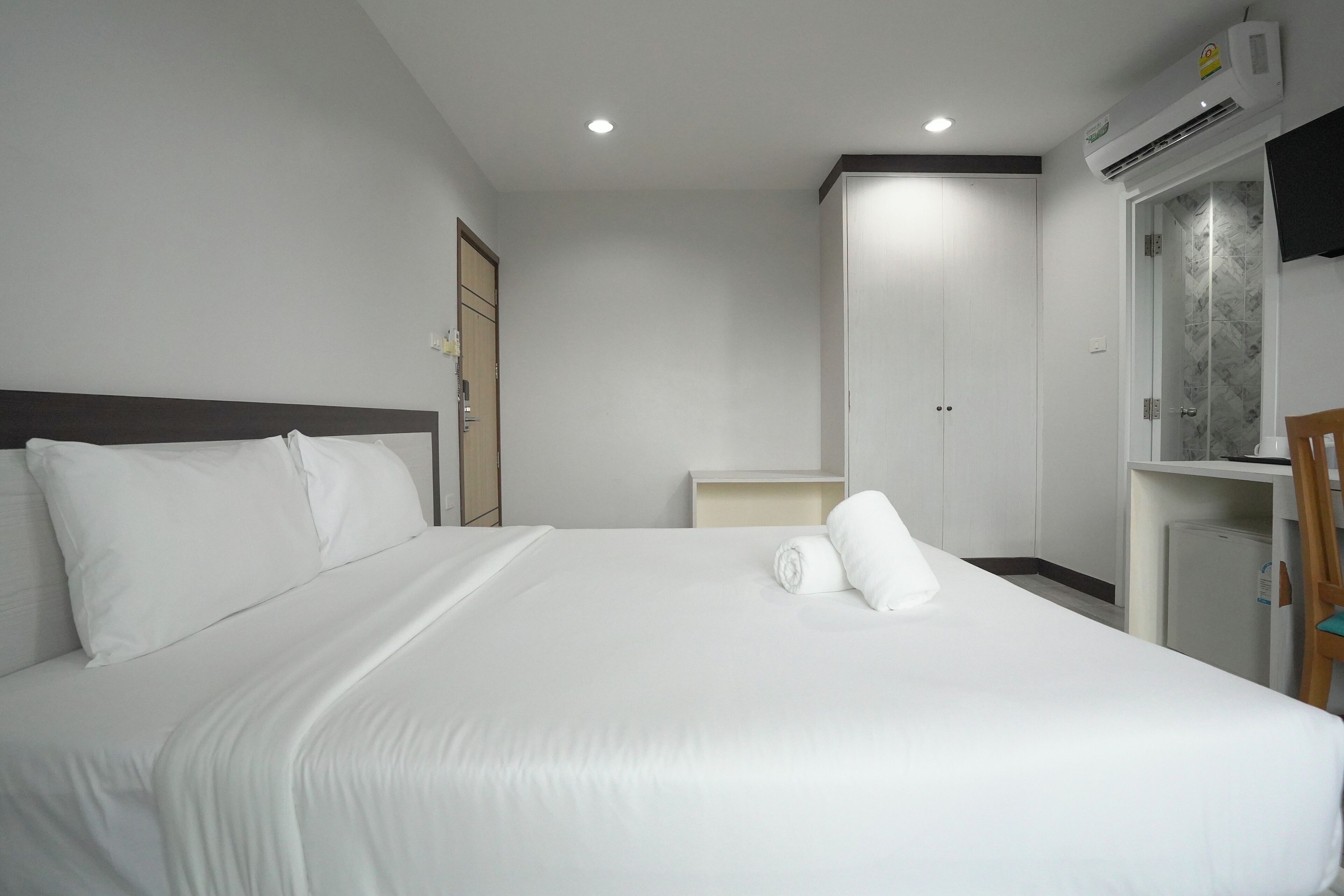 A hotel room with a large bed, a wardrobe, a desk, and an air conditioning unit.