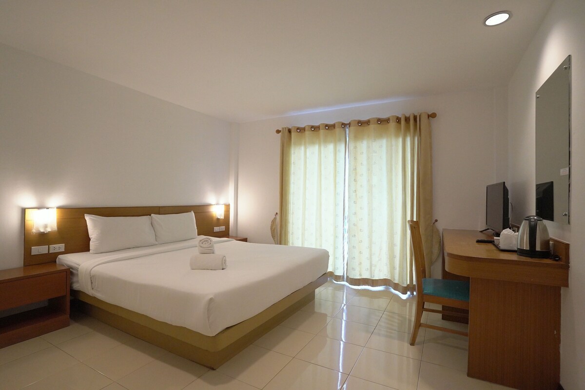 A hotel room with a bed, bedside table, desk, chair, and a large mirror.
