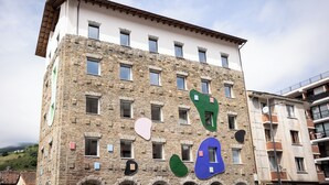 Un edificio de varios pisos con fachada de piedra, varias ventanas y una bandera en la parte superior.