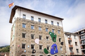 A multi-story building with a stone facade, multiple windows, and a flag on top. - Hotel Truita (Cangas del Narcea)