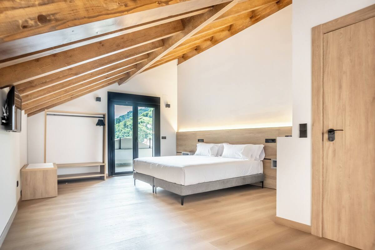 Une chambre avec un lit, des poutres en bois au plafond, une porte et une vue à travers une porte vitrée.