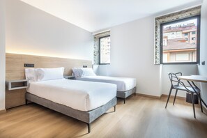 Une chambre d’hôtel moderne équipée de deux lits simples, d’un bureau et d’une chaise.