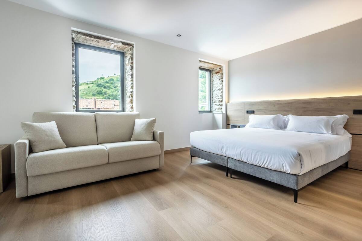 Une chambre à coucher comprenant un lit, un canapé et deux fenêtres donnant sur un paysage verdoyant.