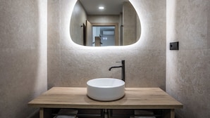 Un baño con un lavabo redondo, un espejo y una encimera de madera.
