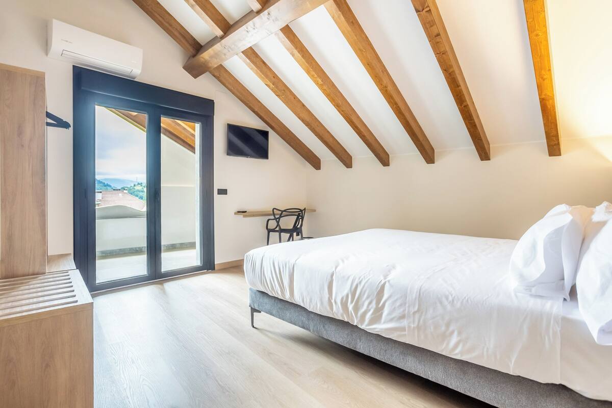 Une chambre à coucher avec un lit, une télévision, un plafond en bois et une porte coulissante donnant sur un balcon.
