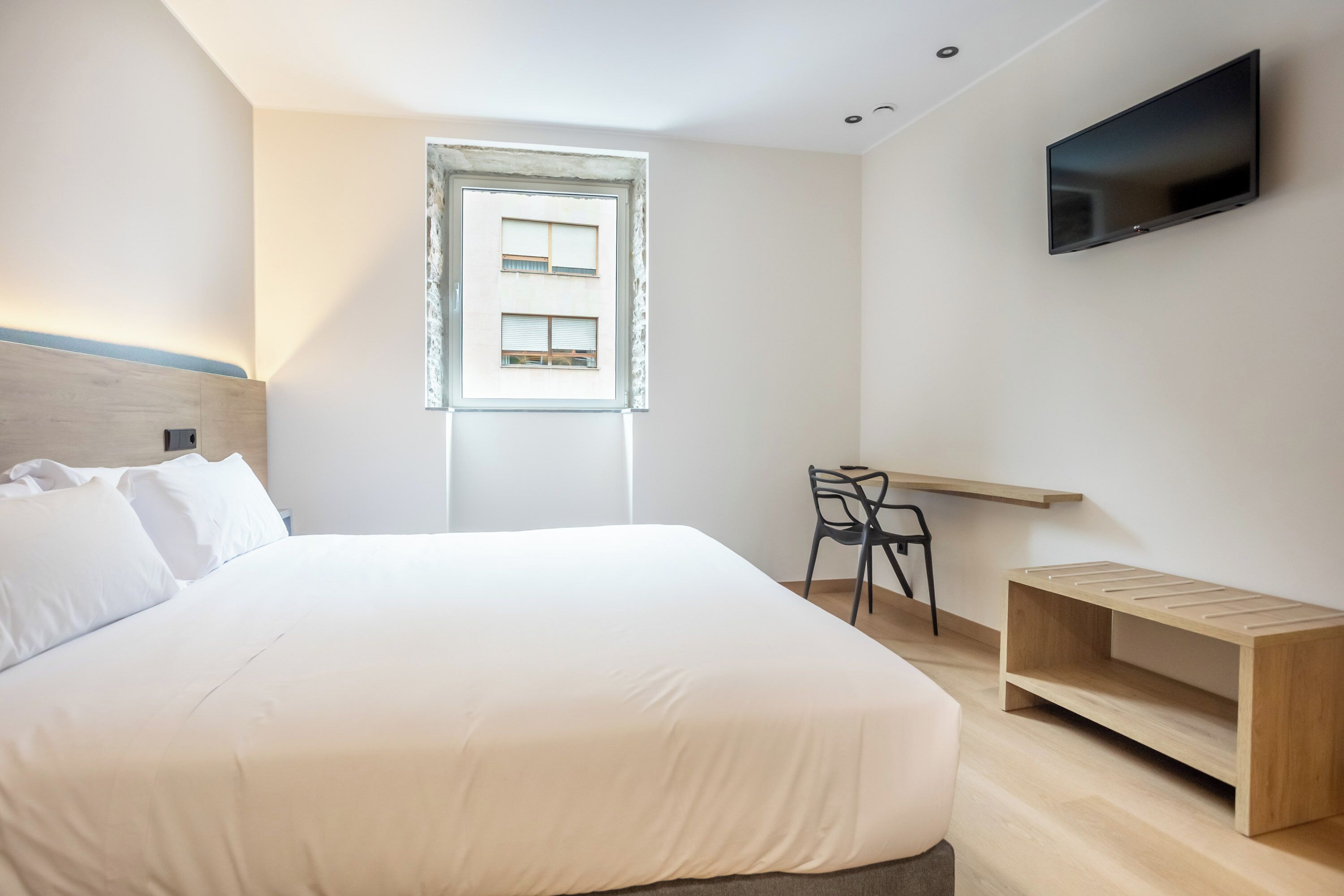 Moderni hotellihuone, jossa on suuri sänky, työpöytä, tuoli, televisio ja ikkuna, jossa on sälekaihtimet.