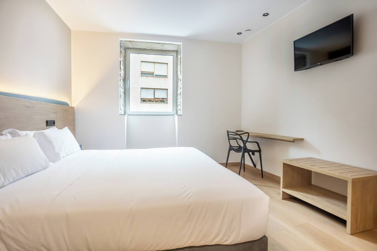 Une chambre d’hôtel moderne équipée d’un grand lit, d’un bureau, d’une chaise, d’une télévision et d’une fenêtre avec des stores.