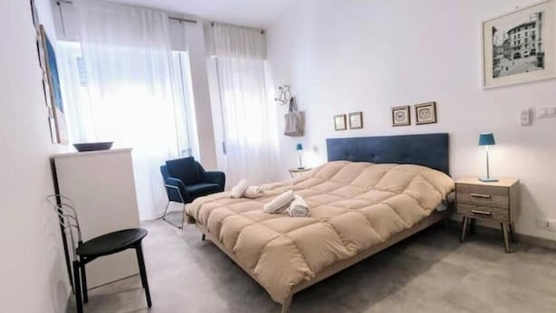 Ein Schlafzimmer mit Bett, Stuhl, Schreibtisch, Nachttisch und einem Fenster mit Vorhängen.