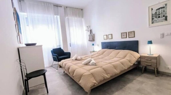 A bedroom with a bed, a chair, a desk, a nightstand, and a window with curtains. - Hostdomus - Sun House (Finale Ligure)