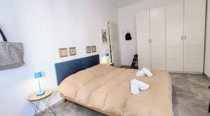 A bedroom with a bed, a wardrobe, a lamp, and a small table. - Hostdomus - Sun House (Finale Ligure)