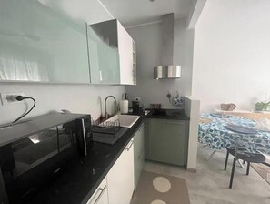 A modern kitchen with a black countertop, a sink, and a small dining area with a table and chairs. - Hostdomus - Sun House (Finale Ligure)