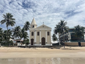 A church with a bell tower, surrounded by palm trees and a sandy beach. - Piratas do Caribe - Casa das Conchas (Tamandaré)