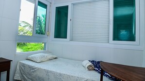 A small room with a bed, two windows with blinds, and a view of greenery outside. - Piratas do Caribe - Casa das Conchas (Tamandaré)