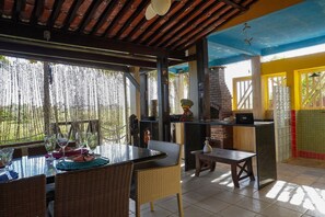 Un comedor al aire libre con sillas de mimbre, una mesa de vidrio y un horno de ladrillo.