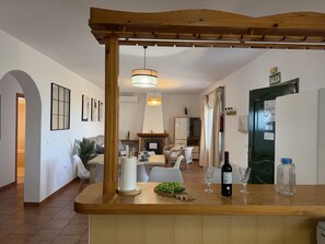Une cuisine moderne avec un comptoir en bois, un luminaire suspendu et un coin repas à l’arrière-plan.