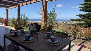 A covered patio with a table set for two, outdoor seating, and a view of the sea. - Cortijo del Verdial by At Home Costa del Sol (Torrox)