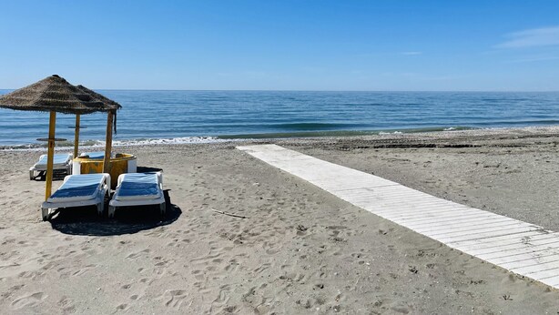 A beach with a thatched-roof structure, two lounge chairs, and a wooden walkway. - Cortijo del Verdial by At Home Costa del Sol (Torrox)