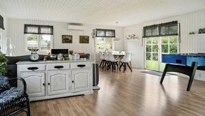 A room with a white cabinet, a foosball table, a dining table with chairs, and a sofa.