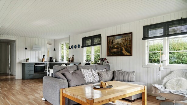 A modern living room with a grey sofa, wooden coffee table, and a dining area.