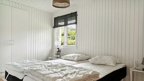 A bedroom with a bed, a window with a black blind, a bedside table with a lamp, and a hanging light fixture.