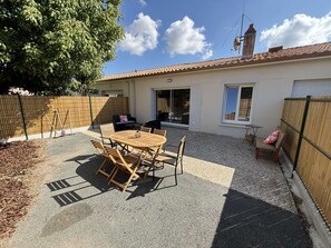 A patio with a round wooden table and chairs, a sliding glass door, and a fenced backyard. - Maison médis 2 bedrooms, sleeps 6 (Médis)