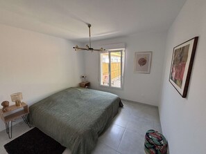 A bedroom with a bed, a small bedside table, a nightstand, a window, and a door. - Maison médis 2 bedrooms, sleeps 6 (Médis)