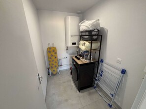 A compact laundry room with a washing machine, ironing board, and drying rack. - Maison médis 2 bedrooms, sleeps 6 (Médis)
