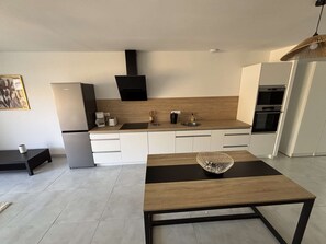 A modern kitchen with white cabinetry, a black countertop, a built-in oven, and a dining table with a woven centerpiece. - Maison médis 2 bedrooms, sleeps 6 (Médis)