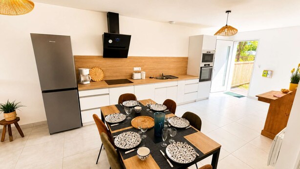 Een moderne keuken met een eethoek, inclusief een koelkast, fornuis en een eettafel gedekt met borden en glazen.