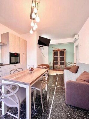 A compact living space with a dining area, kitchenette, and seating area. - Hostdomus - Tiffany House (Finale Ligure)