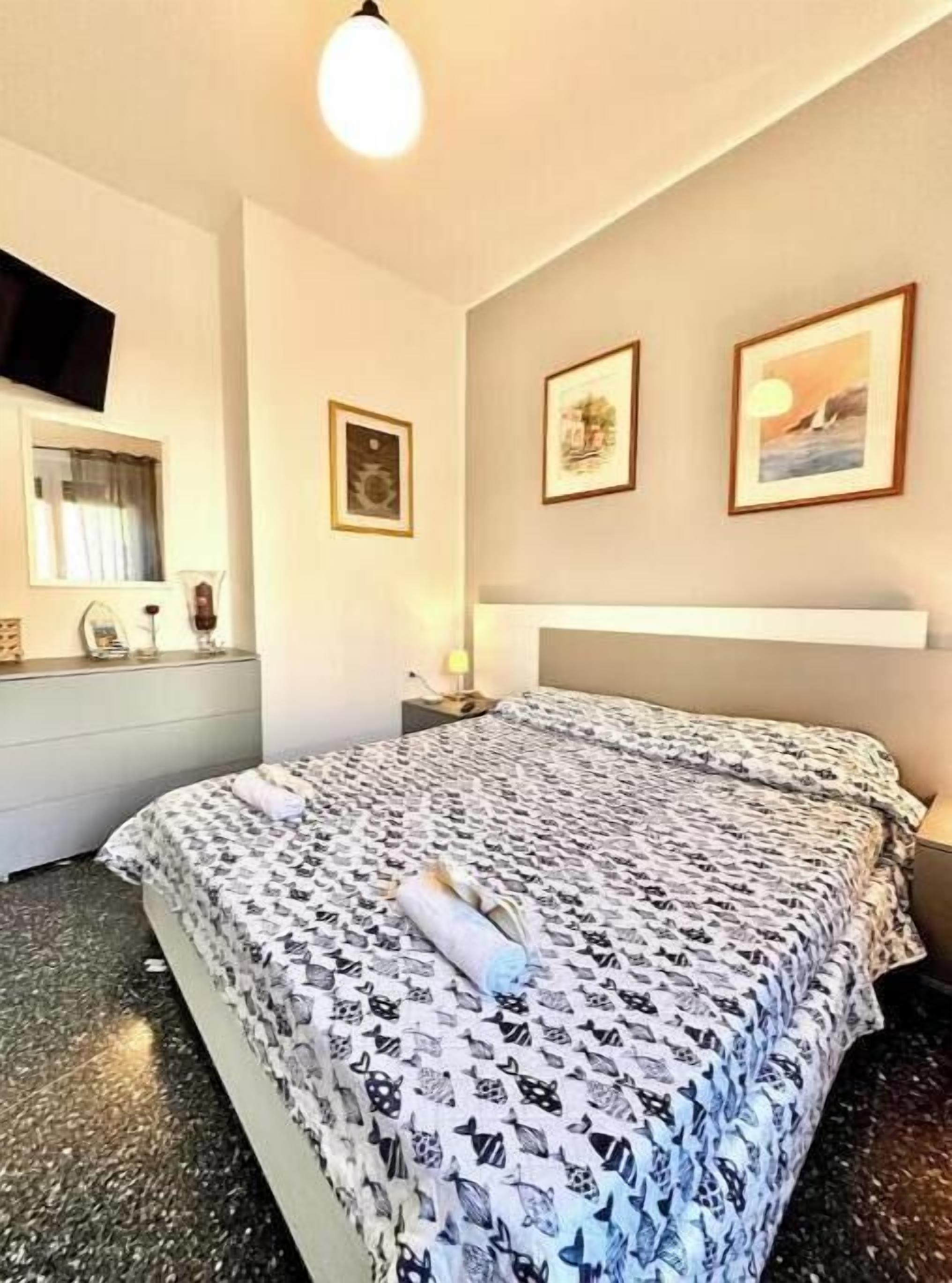 A hotel room with a bed, a bedside table, a lamp, and framed pictures on the wall.