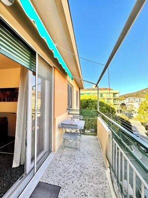 A balcony with a table and chairs, a sliding glass door, and a view of a building and trees. - Hostdomus - Tiffany House (Finale Ligure)