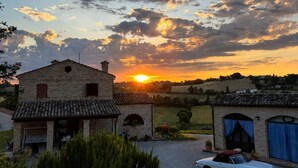 Ländliche Landschaft bei Sonnenuntergang, ein Steinhaus und ein weißes Auto davor geparkt.
