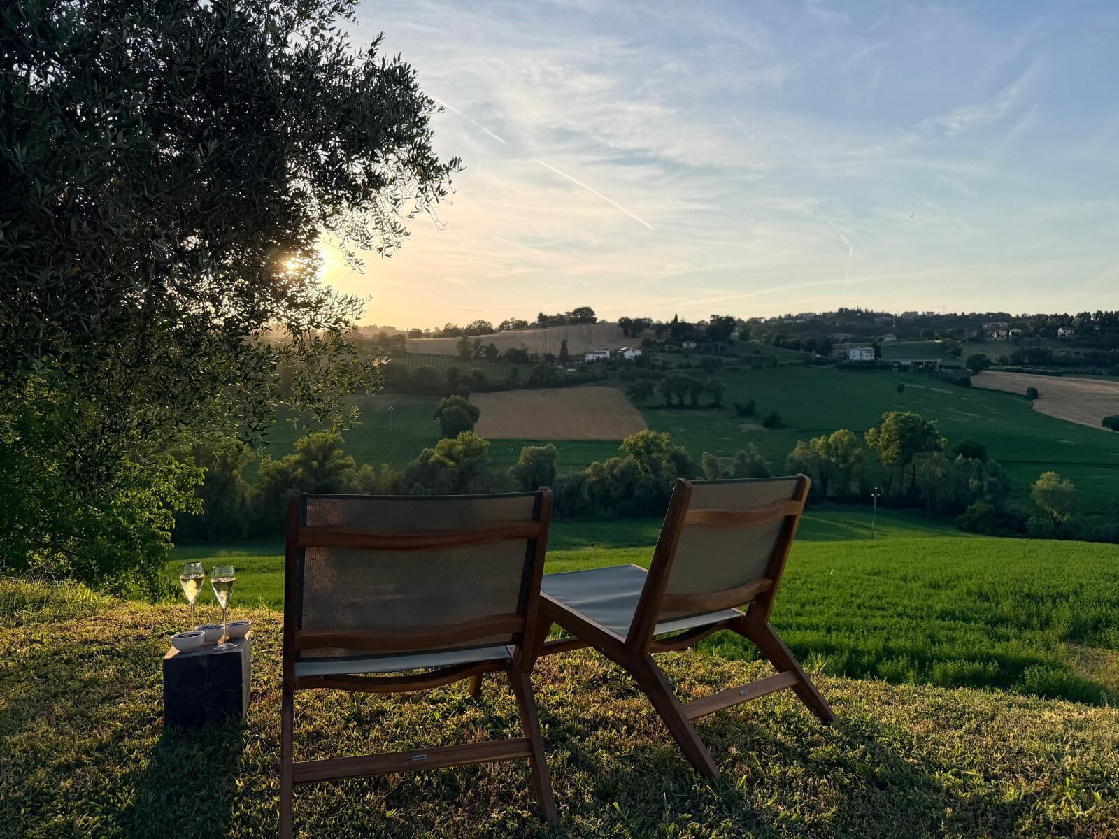 Two chairs with a table, a glass of wine, and a view of a countryside landscape.