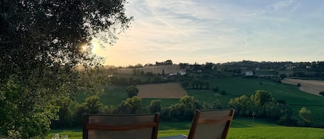Two chairs with a table, a glass of wine, and a view of a countryside landscape.