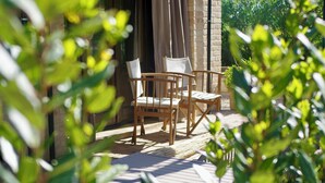 Eine Holzterrasse mit zwei Stühlen und einem Tisch, umgeben von viel Grün.