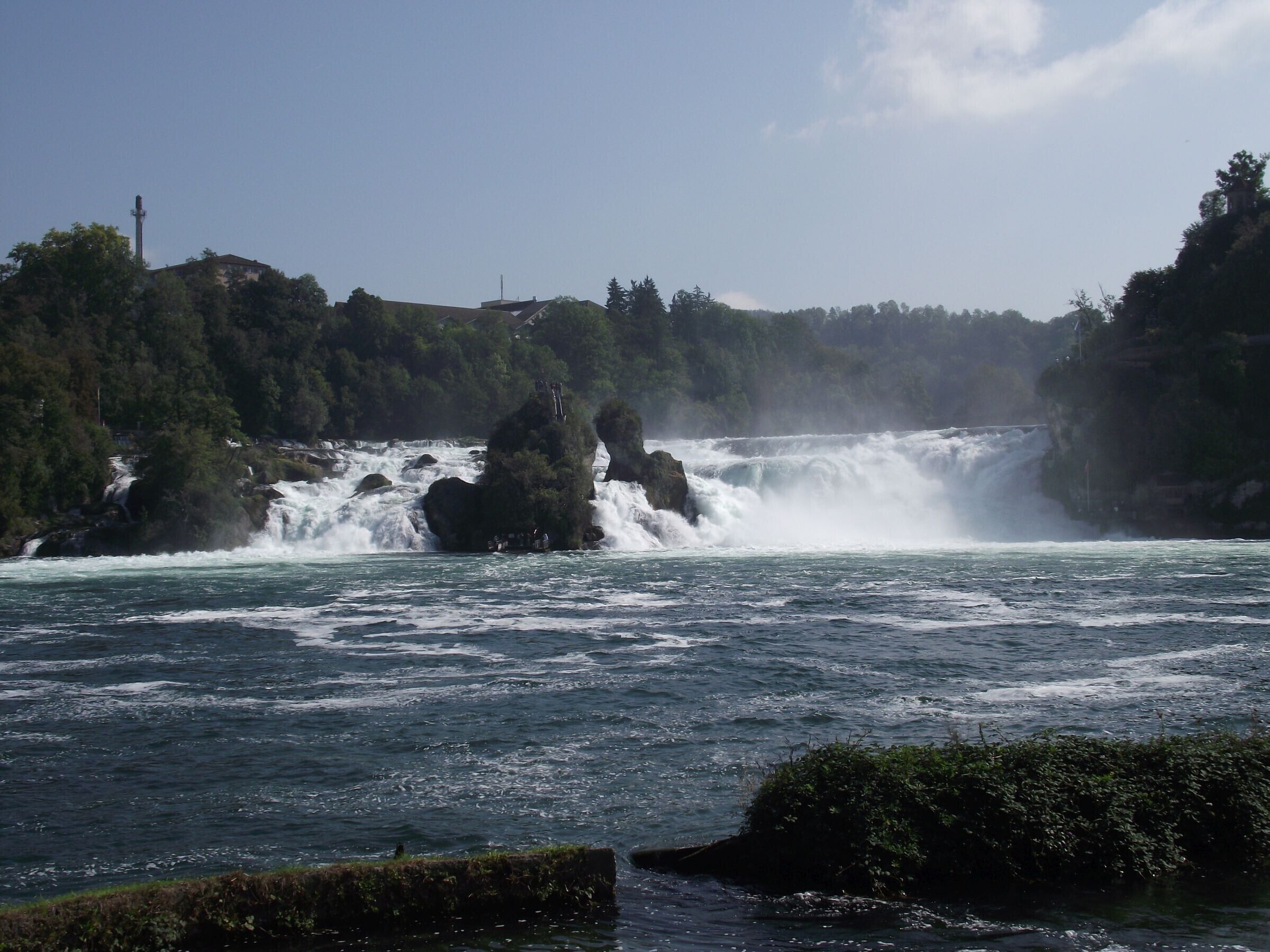 Un río con una cascada, rodeado de vegetación y afloramientos rocosos.