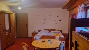 A cozy room with a wooden ceiling, a bed with floral bedding, a round wooden table with chairs, and a wall with a heart-themed decoration. - Shared Room with Shower, WC, and Wi-Fi (Sipplingen)