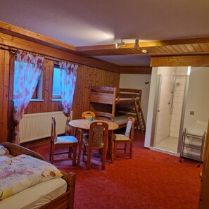 A room with a bunk bed, a table with chairs, a radiator, a shower area, and a window with curtains. - Shared Room with Shower, WC, and Wi-Fi (Sipplingen)