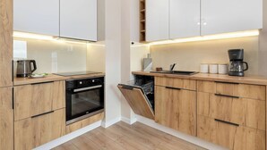 Een moderne keuken met houten kastjes, een vaatwasser, een oven en een koffiezetapparaat.