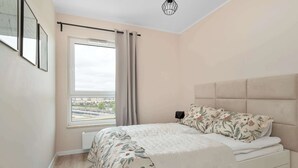 Een slaapkamer met een bed, een raam met gordijnen, een radiator en een wandlamp.