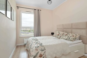 Een slaapkamer met een bed, een raam met gordijnen, een radiator en een wandlamp.