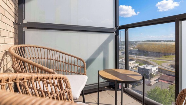 Een balkon met rieten meubilair, een glazen wand en uitzicht op een stadion.