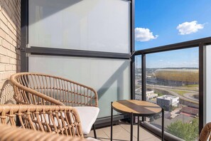 En balkon med fletningsmøbler, glasvæg og udsigt til et stadion.