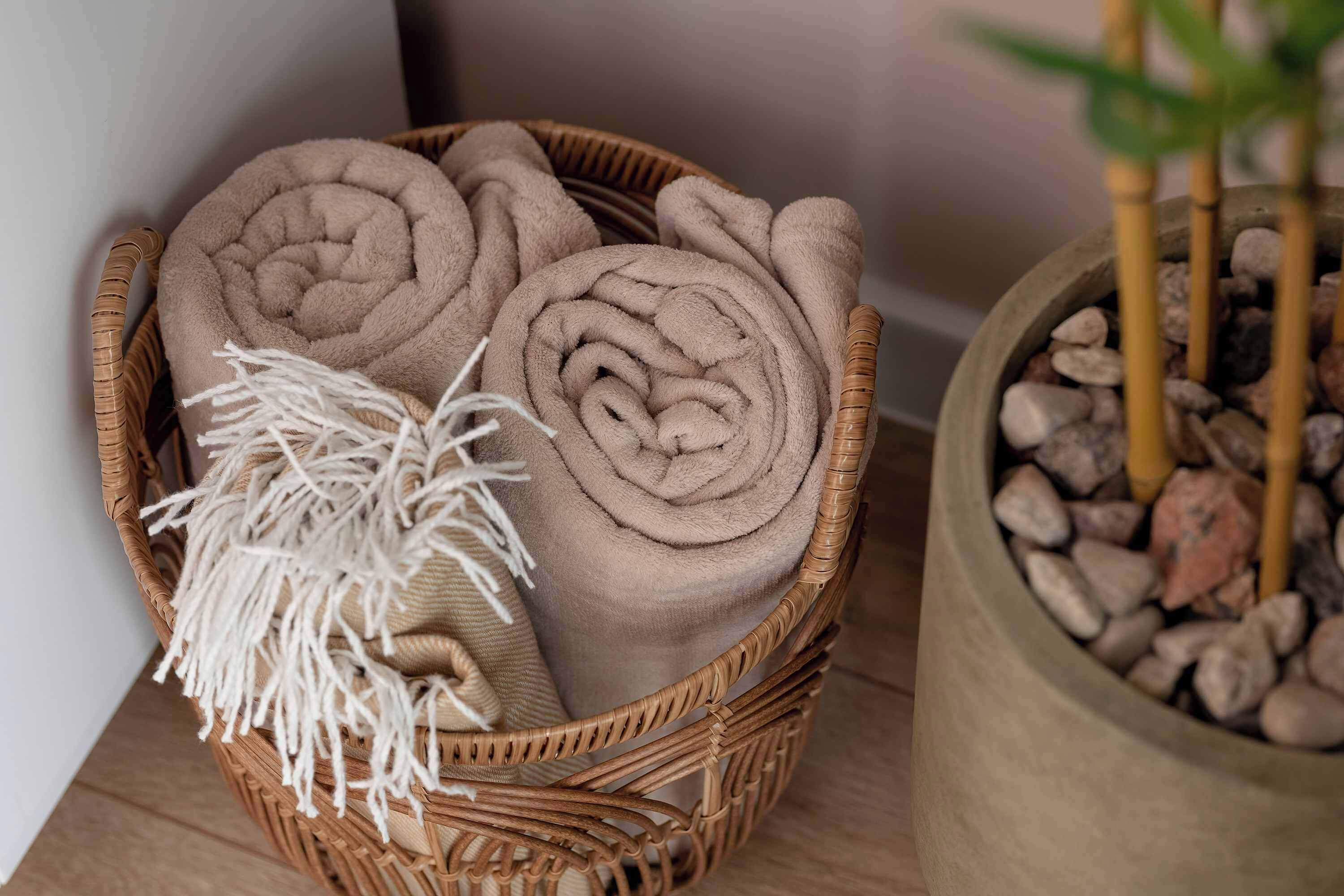 Una cesta de mimbre con toallas dobladas y un chal de macramé.